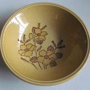 May include: A brown and yellow ceramic bowl with a floral design. The bowl has a wide rim and a rounded bottom. The floral design features brown flowers with yellow centers and brown leaves.