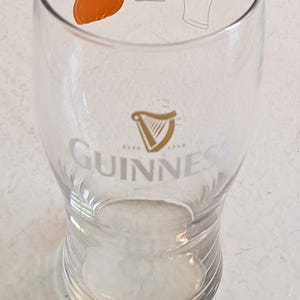 May include: A clear Guinness pint glass with a pumpkin graphic and the equation "pumpkin = beer". The Guinness logo and harp are visible. The glass is designed for beer.