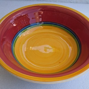 May include: A yellow ceramic bowl with red, green, and blue stripes around the rim.