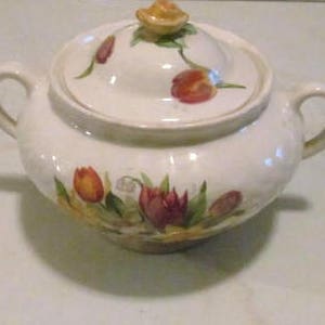 May include: White ceramic sugar bowl with a lid, featuring a floral design with tulips, leaves, and a small bird on the lid.