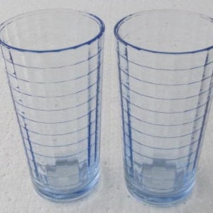 May include: Two tall, clear blue glass drinking glasses with a ribbed pattern. The glasses are empty.