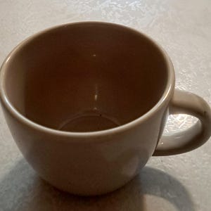 May include: A plain, off-white ceramic coffee mug with a rounded handle.