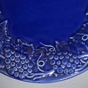 May include: A blue ceramic plate with a white grapevine design. The plate has a raised rim and a smooth surface.