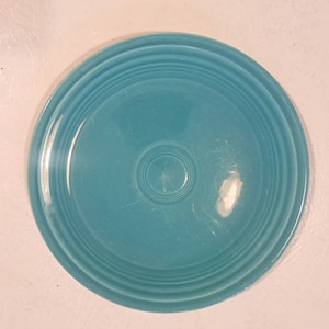 May include: A turquoise blue ceramic plate with a concentric circle design. The plate has a smooth, glossy finish.
