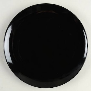 May include: A circular dinner plate with a solid, glossy black finish. The plate features a smooth, reflective surface and a slightly raised rim, presenting a clean, uniform appearance. The design is simple and functional, with no patterns or textures.