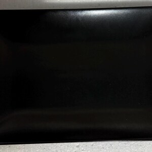 May include: A rectangular black plate with rounded corners. The plate has a smooth, glossy surface and appears to be made of ceramic or a similar material. The plate is empty and ready for use.