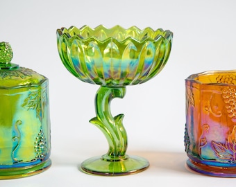 May include: Three iridescent glass candy dishes with a grapevine design. The dishes are green, amber, and clear with a rainbow sheen.