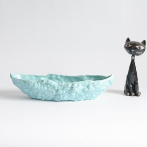 May include: A light blue ceramic planter shaped like a leaf with a textured floral design.