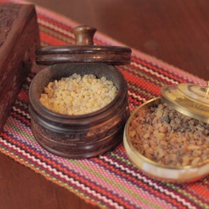 May include: Two wooden containers filled with different types of resin. The containers are on a colorful striped fabric.