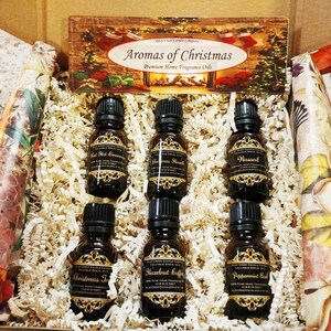 May include: A set of six small brown glass bottles with gold labels containing essential oils. The labels feature the text "Ryley Creek Candle Company" and various Christmas scents, including "Red Hot Cinnamon", "Christmas Hearth", "Wassail", "Christmas Tree", "Hazelnut Coffee", and "Peppermint Bark".
