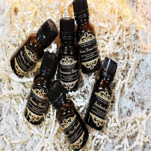 May include: Six small brown glass bottles with black lids and gold labels. The labels have different scents listed on them, including "Cinnamon Bun", "Lemon Pound Cake", "Blueberry Cobbler", "Caramel Bread", "Nut Bread", and "Snickerdoodle".