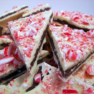 May include: A close-up of a pile of white chocolate bark broken into pieces. The bark is topped with crushed candy canes and a layer of dark chocolate.