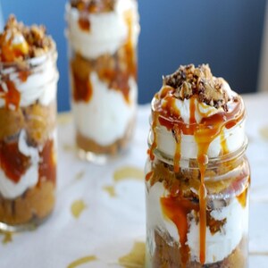 May include: Three glass jars filled with a layered dessert. The dessert is made with pumpkin, whipped cream, caramel sauce, and a crunchy topping.