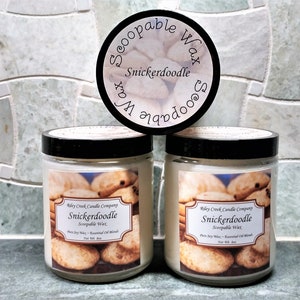 May include: Three glass jars of "Snickerdoodle" scented soy wax candles with a scoop of wax on top. The jars have black lids and labels that say "Riley Creek Candle Company" and "Snickerdoodle Scoop-able Wax".