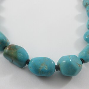 May include: A turquoise necklace with large, irregular shaped beads. The beads are strung on a black cord.