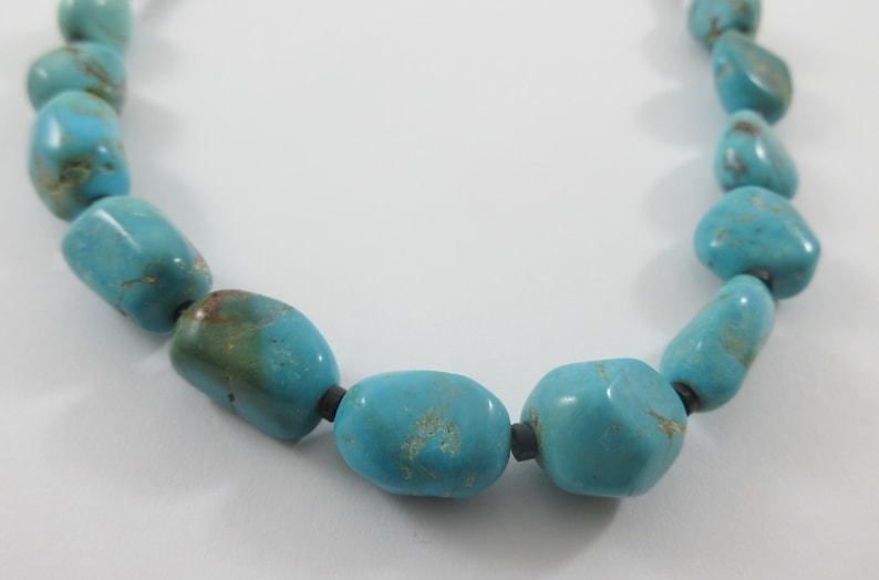 May include: A turquoise necklace with large, irregular shaped beads. The beads are strung on a black cord.