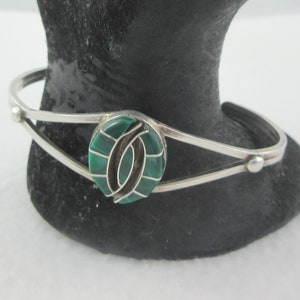 May include: A silver bracelet featuring a green malachite stone set within a silver circle. The stone is encircled by a silver design.