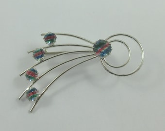 May include: A silver brooch with a central iridescent blue, green, and pink rhinestone surrounded by three concentric circles. Five smaller iridescent rhinestones are attached to curved silver wires radiating from the center.