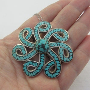 Pu&ograve; includere: Una collana con un ciondolo in argento a forma di fiore turchese. Il fiore &egrave; realizzato con un'intricata lavorazione in argento ed &egrave; incastonato con pietre turchesi.