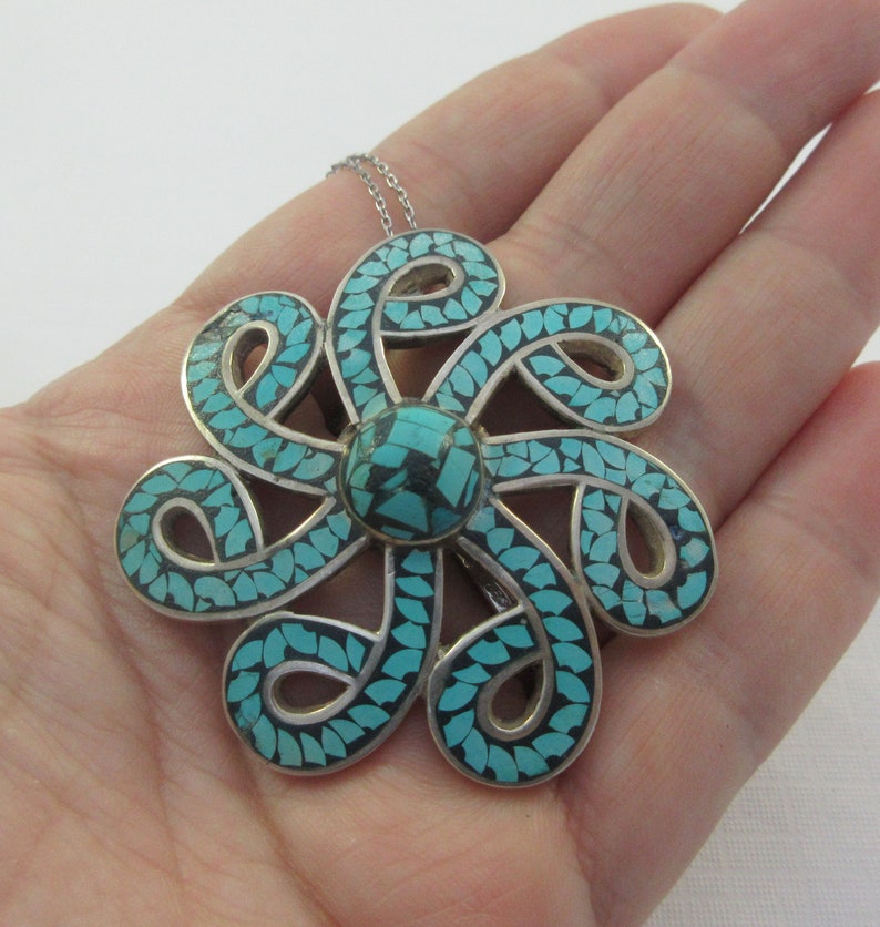 Pu&ograve; includere: Una collana con un ciondolo in argento a forma di fiore turchese. Il fiore &egrave; realizzato con un'intricata lavorazione in argento ed &egrave; incastonato con pietre turchesi.