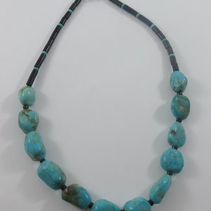 May include: A turquoise and black beaded necklace with a silver clasp. The necklace is made of large, irregular turquoise stones separated by small black beads.