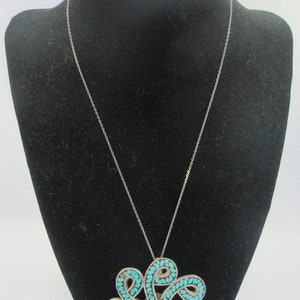 Pu&ograve; includere: Una collana con catena d'argento con un ciondolo in turchese. Il ciondolo &egrave; un grande e intricato design di pietre turchesi incastonate in argento.