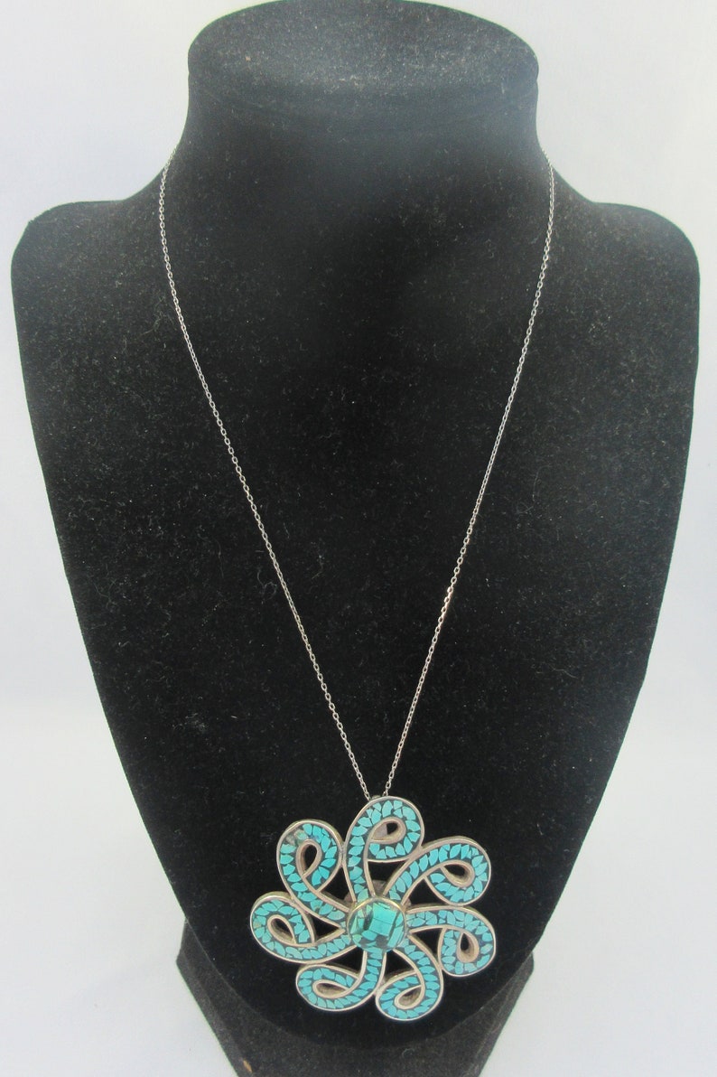 Pu&ograve; includere: Una collana con catena d'argento con un ciondolo in turchese. Il ciondolo &egrave; un grande e intricato design di pietre turchesi incastonate in argento.