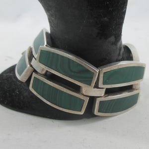 May include: Silver-toned bracelet with rectangular malachite inlays. The bracelet is composed of connected links, each featuring a polished silver frame and a vibrant green stone. The bracelet is displayed on a black velvet surface.