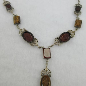 May include: A silver necklace with a cameo pendant and multiple brown and white stones. The necklace features a delicate filigree design.