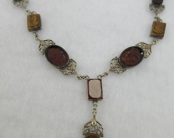 May include: A silver necklace with a cameo pendant and multiple brown and white stones. The necklace features a delicate filigree design.