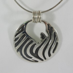 May include: A silver necklace with a round pendant featuring a stylized abstract design. The pendant has a textured surface and a cutout in the center.