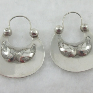 May include: A pair of silver hoop earrings with a crescent moon design and intricate etched details.