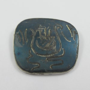 May include: An oval silver brooch with a blue enamel background and a silver design of a stylised bird with a wavy line pattern.