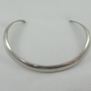 May include: A silver choker necklace with a smooth, rounded surface.