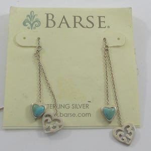May include: Silver dangle earrings with turquoise heart-shaped stones and openwork heart charms. The earrings are displayed on a light yellow card with the brand name "BARSE" and the words "STERLING SILVER".