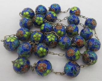 Puede incluir: Un collar largo con cuentas de esmalte azul decoradas con flores de colores. Las cuentas están conectadas por una cadena de plata.