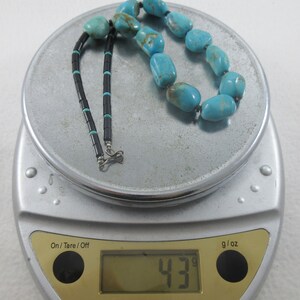 May include: A turquoise and black beaded necklace with a silver clasp, weighing 43 grams on a digital scale.