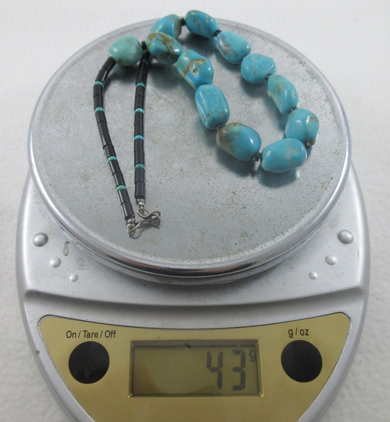 May include: A turquoise and black beaded necklace with a silver clasp, weighing 43 grams on a digital scale.