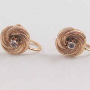May include: A pair of gold-tone earrings with a swirl design and a clear rhinestone in the centre.