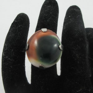 May include: A silver ring with a large oval-shaped green, brown, and white stone set in the center.