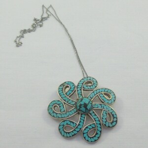 Pu&ograve; includere: Una collana d'argento con un ciondolo in turchese e argento a forma di fiore. Il ciondolo &egrave; composto da molti piccoli pezzi di turchese incastonati in argento.