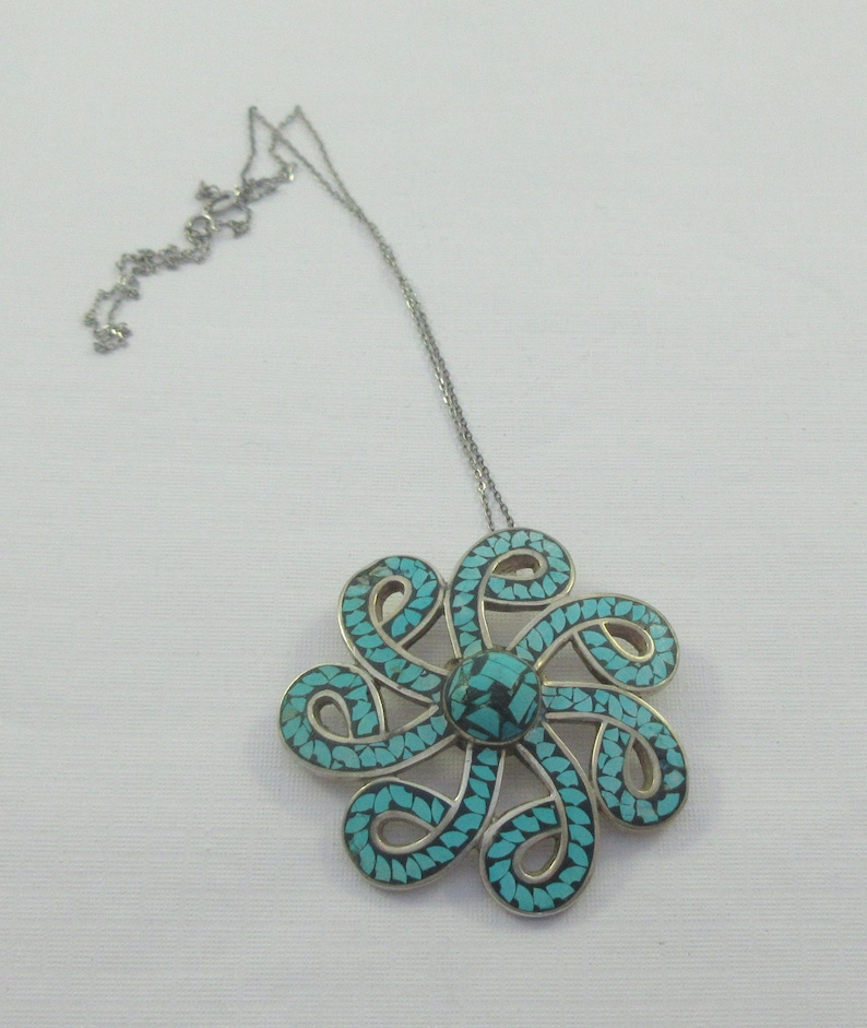 Pu&ograve; includere: Una collana d'argento con un ciondolo in turchese e argento a forma di fiore. Il ciondolo &egrave; composto da molti piccoli pezzi di turchese incastonati in argento.