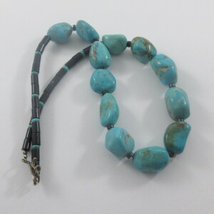 May include: A turquoise and black beaded necklace with a silver clasp. The necklace is made of large, irregular turquoise stones and small, black beads.