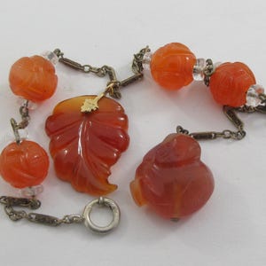 May include: An antique bracelet featuring carved orange-red gemstone beads and pendants. The bracelet includes a leaf-shaped pendant, round beads, and a bird-shaped pendant, all connected by metal chain links and clear crystal beads.