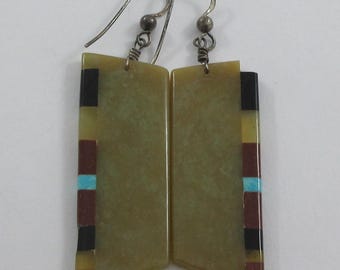 May include: A pair of rectangular earrings with silver hooks. The earrings have a light green background with a decorative pattern of black, brown, yellow, and turquoise rectangles. The earrings are displayed against a white background.