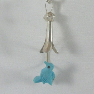 May include: A silver pendant necklace with a turquoise bird charm. The pendant is shaped like a flower with a long stem.