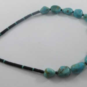 May include: A turquoise and black beaded necklace with a silver clasp. The necklace features large, irregular turquoise stones.