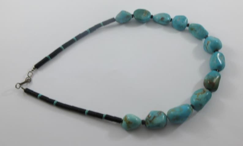 May include: A turquoise and black beaded necklace with a silver clasp. The necklace features large, irregular turquoise stones.