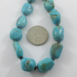May include: A turquoise gemstone necklace with black beads. The necklace is laid out on a white surface with a US quarter for scale.