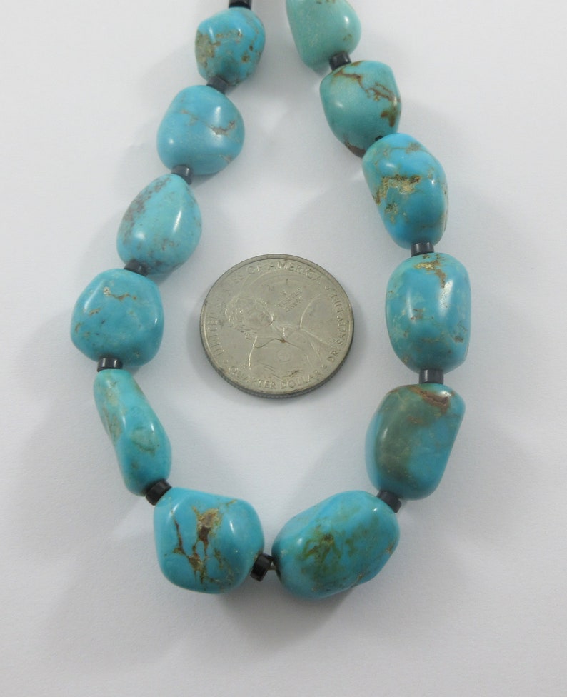 May include: A turquoise gemstone necklace with black beads. The necklace is laid out on a white surface with a US quarter for scale.